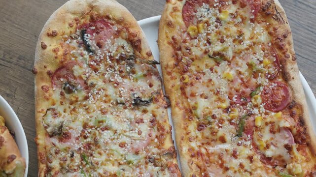 Close-up of sliced rectangular mixed pizza with rich toppings on wooden board