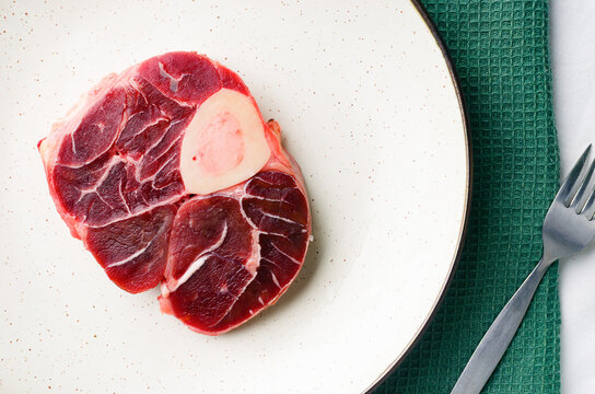 Raw beef shank cross-section with bone and marrow on a white plate.