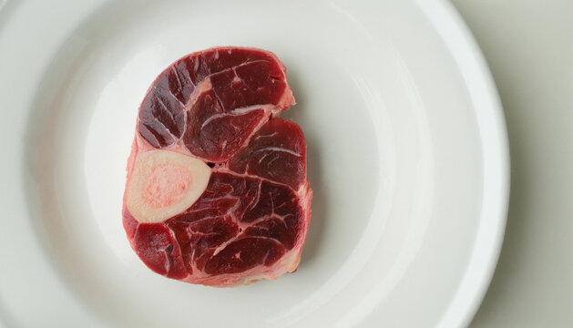 Raw beef shank cross-section with bone marrow on a white plate.
