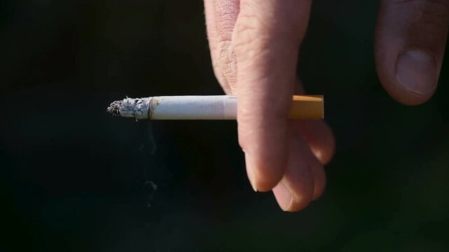 Close Up of Male Hand Holding a Burning Cigarette with Smoke