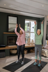 Fototapeta premium Female friends standing on black yoga mats in living room stretching overhead near fireplace mantel