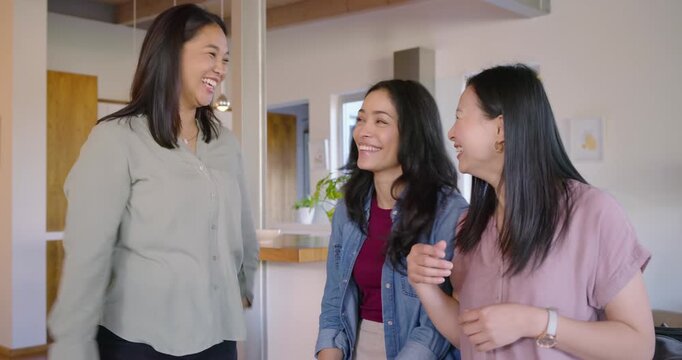 Asian women standing by kitchen island, left woman speaking, others listening and exchanging jokes