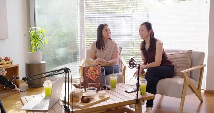 Female cohosts replying to host cue, turning, laughing, gesturing around table with mics in studio