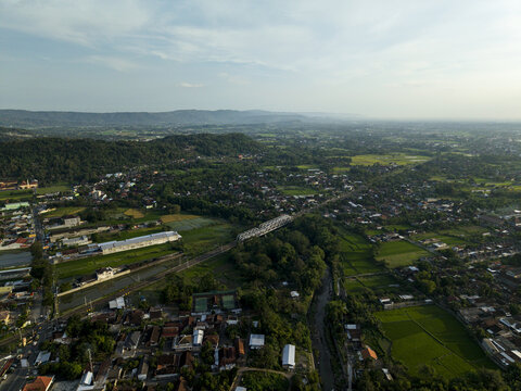 Aerial view of the lush landscape and urban sprawl featuring a bridge over a river and distant hills under a soft sky Kecamatan Prambanan, Daerah Istimewa Yogya, Indonesia.