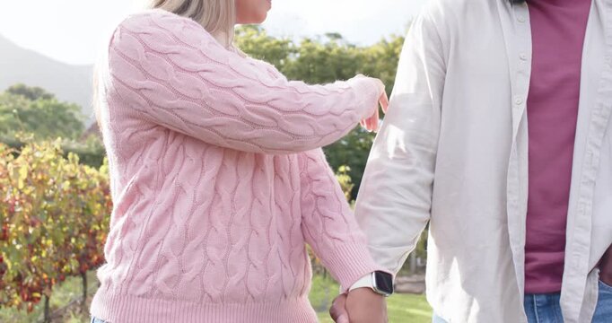 African American couple walking path joined hands, woman sliding watch on his arm, pointing at view