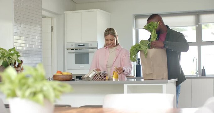 Couple unpacking at kitchen island, bag arriving, man lifting celery, woman prepping jar for meal