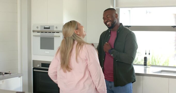 Couple dancing in kitchen while man initiating invite, gesturing near oven, wearing casual clothes