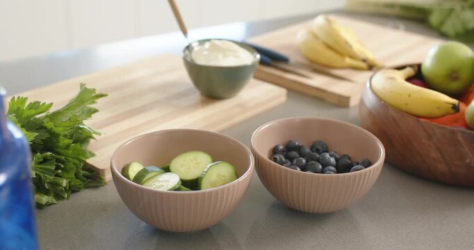 Camera is shifting focus, showing two ceramic bowls with cucumber and blueberries on counter