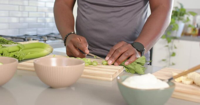 African American couple starting man slicing celery, woman slicing banana, making meal in kitchen