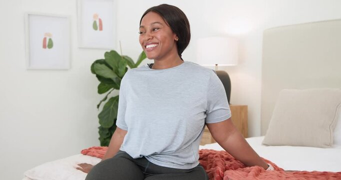 African American woman on bed in bedroom with lapel mic, smiling and laughing at off-camera cue