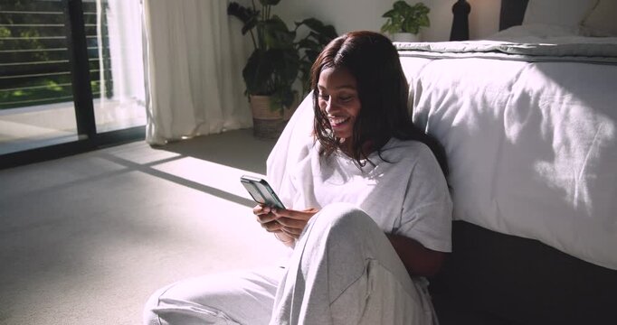 Woman reading message on phone in bedroom, smiling, tapping, leaning back and basking in sun