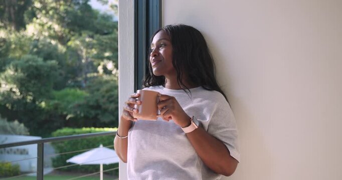 African woman holding tan mug closing eyes pausing gazing out balcony garden smiling, copy space