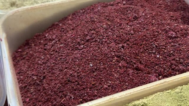 Aromatic sumac seasoning with rich burgundy powder texture stored in spice container for natural culinary use and flavorful food preparation.