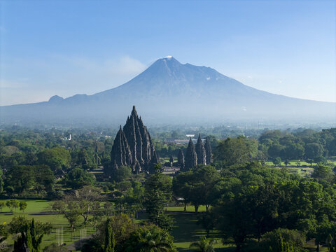 Aerial view of Prambanan Temple complex with stone spires set against Mount Merapi and lush tropical forests in Kecamatan Prambanan, Daerah Istimewa Yogyakarta, Indonesia.