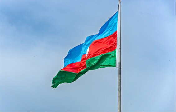 Azerbaijan flag waving on a silver pole against a blue sky with clouds