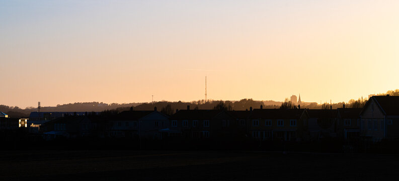 Wide suburban skyline with rooftops under warm fading sunset horizon glow.
