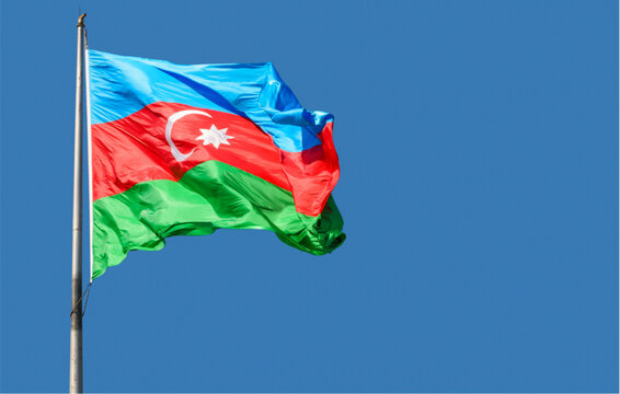 The azerbaijani flag waves on a silver pole against a clear blue sky with a white crescent and star on a red green and blue background