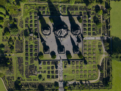 Aerial view of the Prambanan Temple complex with ancient stone spires and long shadows over the green parkland in Kecamatan Prambanan, Daerah Istimewa Yogya, Indonesia.