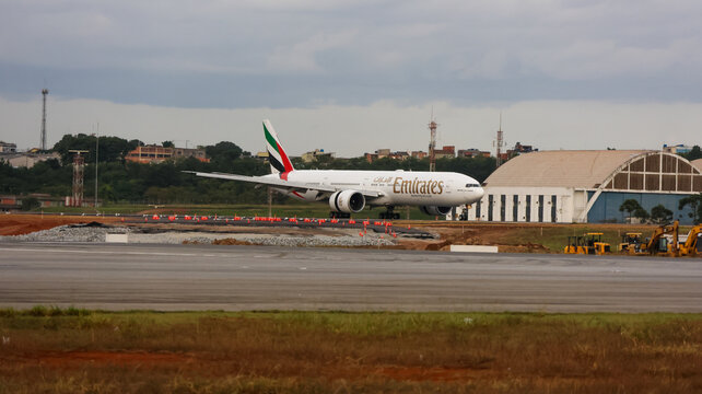 Jato de passageiros da Emirates movimentando-se no Aeroporto de Guarulhos, com pista, &aacute;rea verde e estrutura aeroportu&aacute;ria ao redor. Guarulhos, SP, 10 de maio de 2026.
