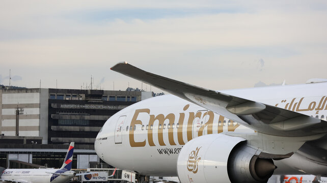 Imagem de aeronave da Emirates no aeroporto de Guarulhos, com a identidade visual da companhia, o grande porte do jato e a paisagem aeroportu&aacute;ria sob nuvens densas. Guarulhos SP 10 Maio 2026