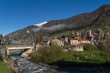 Obraz premium A modern suspension bridge spans the river that flows through Mestia in Georgia.