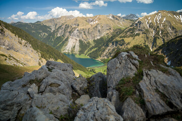 Obraz premium Alpine Lake and Mountain Valley Framed by Rocky Foreground Under Blue Sky