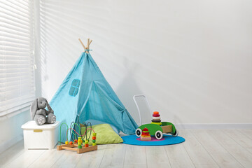 Wigwam, toys and pillows near white wall in child's room, space for text © New Africa