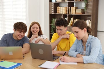 Fototapeta premium Group of students studying with laptops and notebooks at wooden desk in classroom