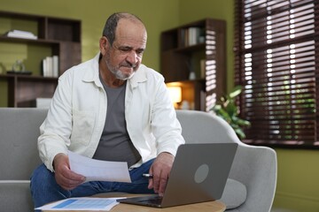 Obraz premium Pension. Senior man with laptop and paperwork at table indoors. Space for text