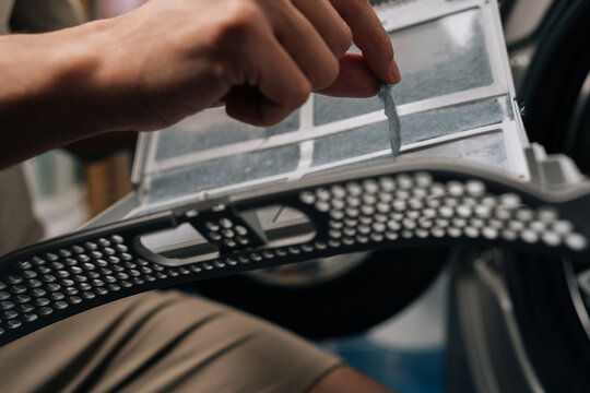Close-up of person removing lint from tumble dryer filter, performing routine household chore and essential appliance maintenance, ensuring proper functioning and preventing fire hazards.