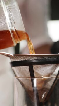 Chef colando ron infusionado con almendras en un frasco de vidrio. Un chef profesional filtra la infusi&oacute;n de ron con almendras a trav&eacute;s de un colador. Preparaci&oacute;n de c&oacute;ctel artesanal, receta moderna.