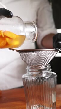 Chef colando alm&iacute;bar de melocot&oacute;n para una receta culinaria moderna. Un chef profesional filtrando alm&iacute;bar casero de melocot&oacute;n con un colador. Conserva artesanal, proceso de gastronom&iacute;a moderna.