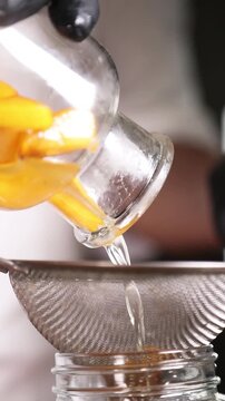 Chef colando alm&iacute;bar de melocot&oacute;n para una receta culinaria moderna. Un chef profesional filtrando alm&iacute;bar casero de melocot&oacute;n con un colador. Conserva artesanal, proceso de gastronom&iacute;a moderna.