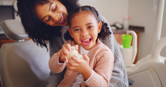 Happy child, mother and tooth model at dentist office for learning oral health, play and excited. Mom, girl and pediatric orthodontics with teeth, typodont and dental care with parent for portrait
