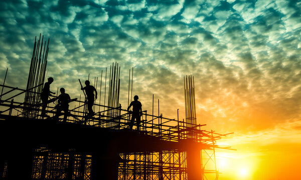Silhouettes of construction workers working on a building site during a dramatic golden sunset