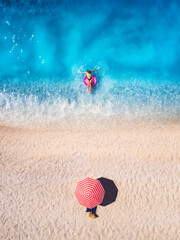Aerial drone view of a woman swimming with pink swim ring in blue sea, sandy beach and red...