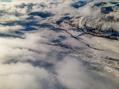 Aerial view of the snow-covered Babusar Pass with a winding mountain road through the valley under thick white clouds Naran, KPK, Pakistan.