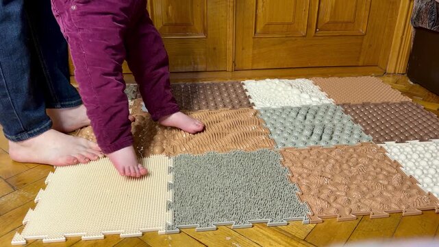 Little child resisting to stand on an orthopedic sensory mat, playful family moment at home.