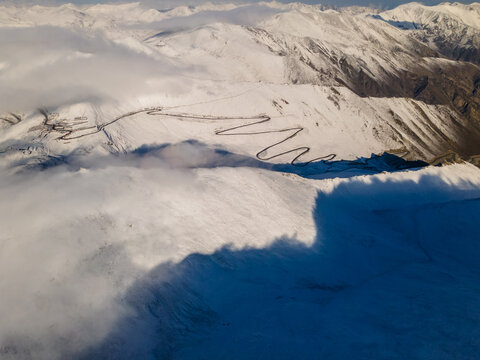 Aerial view of the winding Babusar Pass road snaking through snow-covered mountain peaks and thick clouds in Naran, KPK, Pakistan.