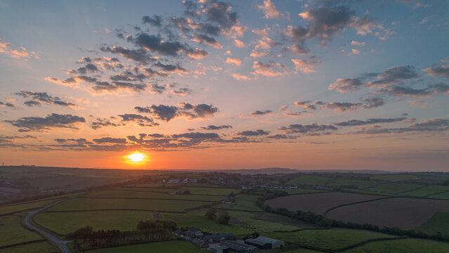 Wide cinematic drone landscape of sunrise over rural Cornwall near Looe featuring golden light, patchwork fields and dramatic clouds across rolling countryside.