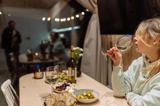 Blonde Woman Drinking White Wine In Cozy Tiny House Kitchen At Night