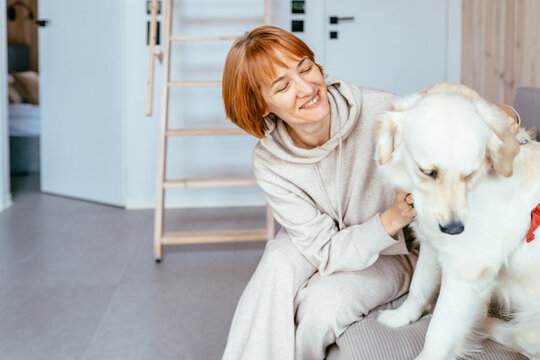 Happy Mature Woman Playing With Golden Retriever In Cozy Tiny House Living Room