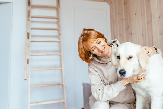 Mature Woman Holding Golden Retriever In Minimal Nordic Cabin Interior