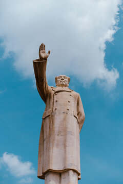 Low angle view of a large stone monument of Chairman Mao Zedong with a raised hand against a blue sky with clouds