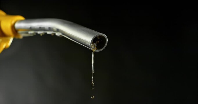 Super slow motion (1000 fps) fuel drops dripping from gasoline nozzle, symbol of depletion and fuel shortage. Minimal liquid flow on black background, dramatic lighting, energy crisis concept.