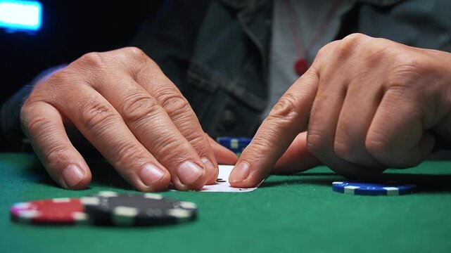 Hands of a male poker player positioned over a green felt table as he reveals an Ace of clubs card, placing chips strategically while surrounded by other poker chips and cards