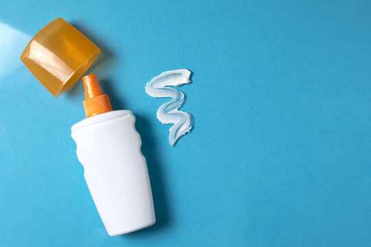 Bottle of sunscreen and texture of cream on colored background top view