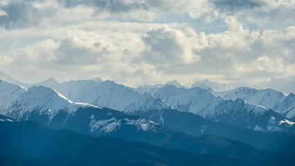 Fototapeta premium Panoramic winter view of the Fagaras Mountains in Transylvania, Romania, with snow-covered Carpathian peaks, layered ridges, clouds and cold alpine atmosphere