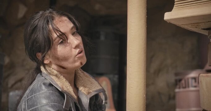 Exhausted, filthy woman in sci-fi area talking to someone off screen and resting on pillar