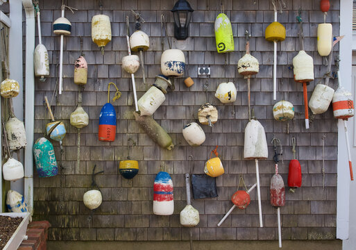 View of numerous colorful and weathered fishing buoys hanging on a grey wooden shingle wall of a coastal building in Martha's Vineyard, Massachusetts